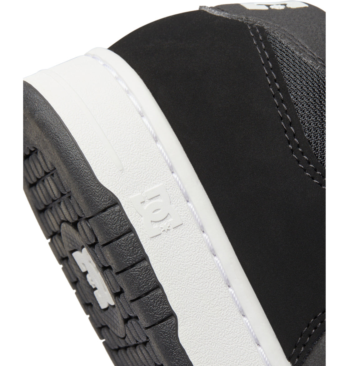 Close-up of a black and white Men’s Manteca 4 Shoe by DC Shoes, showing the heel, sole, and part of the upper. The DC Shoes logo appears on the side of the white midsole and on the black rubber outsole tread, emphasizing its performance-driven design.