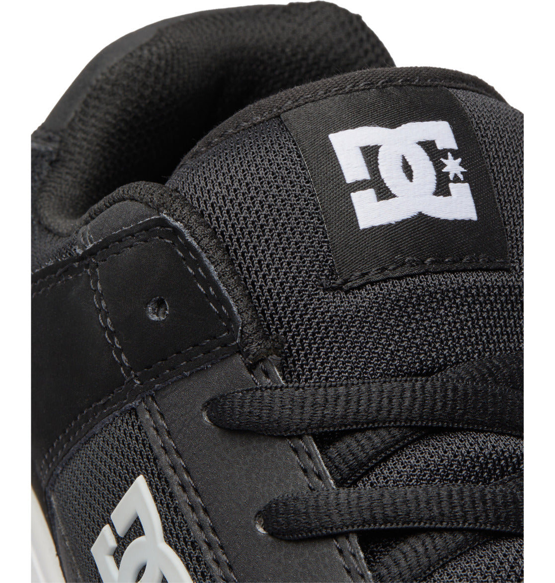Close-up of a black Men’s Manteca 4 Shoe by DC Shoes, featuring the tongue with the white DC Shoes logo and showing part of the laces and stitching detail that emphasize its performance-focused design.