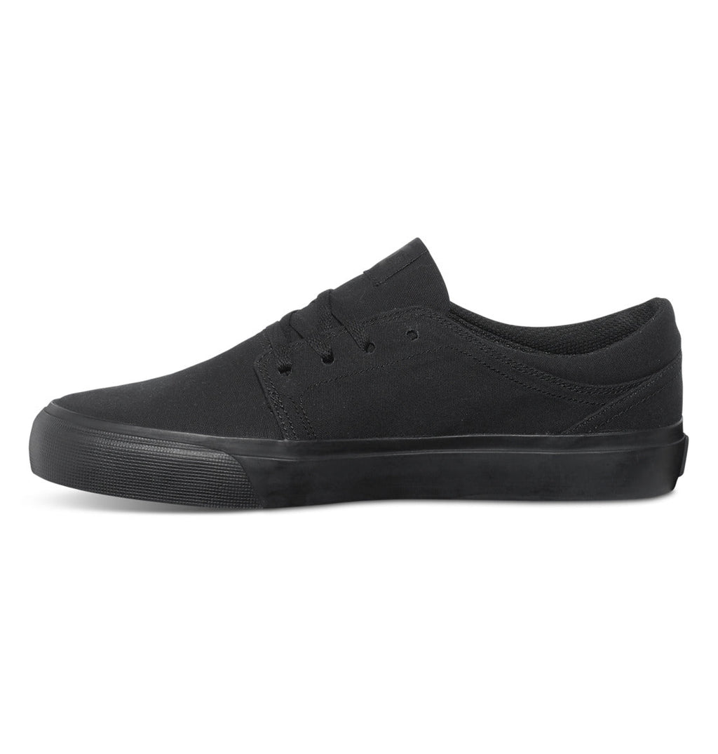 The DC Shoes Men’s Trase Canvas Shoes are featured in black, with a low-top canvas upper, matching black laces, and a black rubber sole. Shown in a side view against a white background, these sneakers highlight their classic skate style and low-profile design.