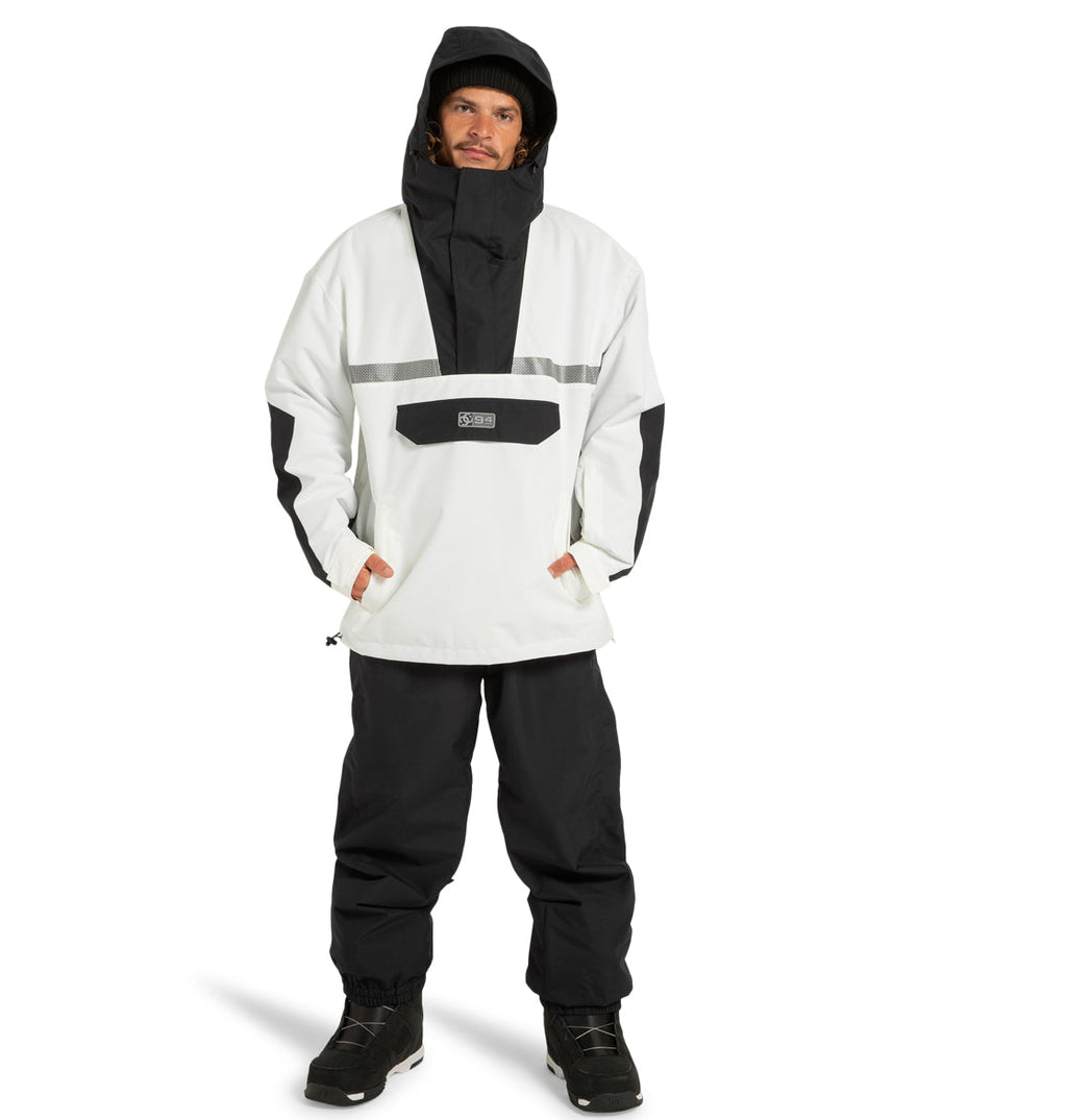 A man stands facing forward against a plain white background, wearing the DC Shoes Mens’ DC-43 Anorak Jacket in black and white—crafted from recycled polyester—paired with matching black pants and black boots.