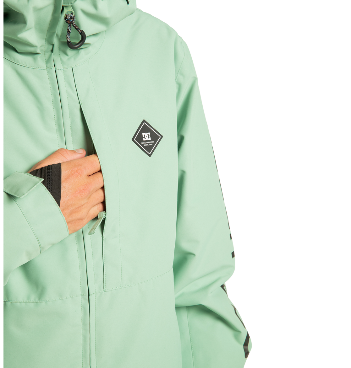 A person wearing the DC Shoes Unisex Basis Insulated Jacket in light green, featuring a diamond-shaped logo on the chest, puts their hand into one of the front zipper pockets. Crafted from recycled polyester, this stylish outerwear is ideal for winter activities. The photo captures the upper body against a white background.