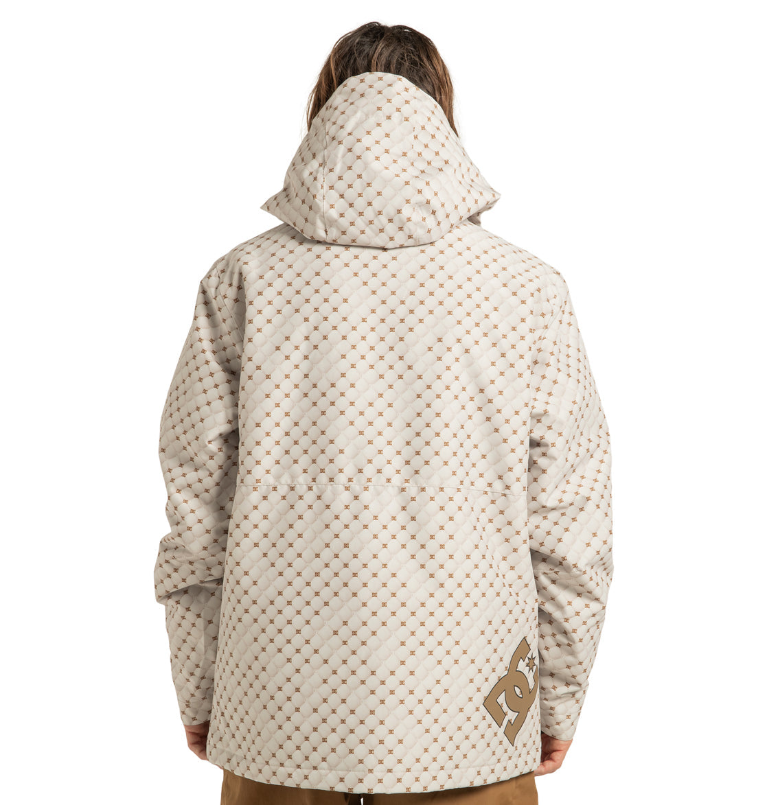 A person is seen from behind wearing the DC Shoes Unisex Basis Print Insulated Jacket, a hooded, patterned beige and white coat made from recycled polyester, featuring the DC logo on the lower right side near the hem.