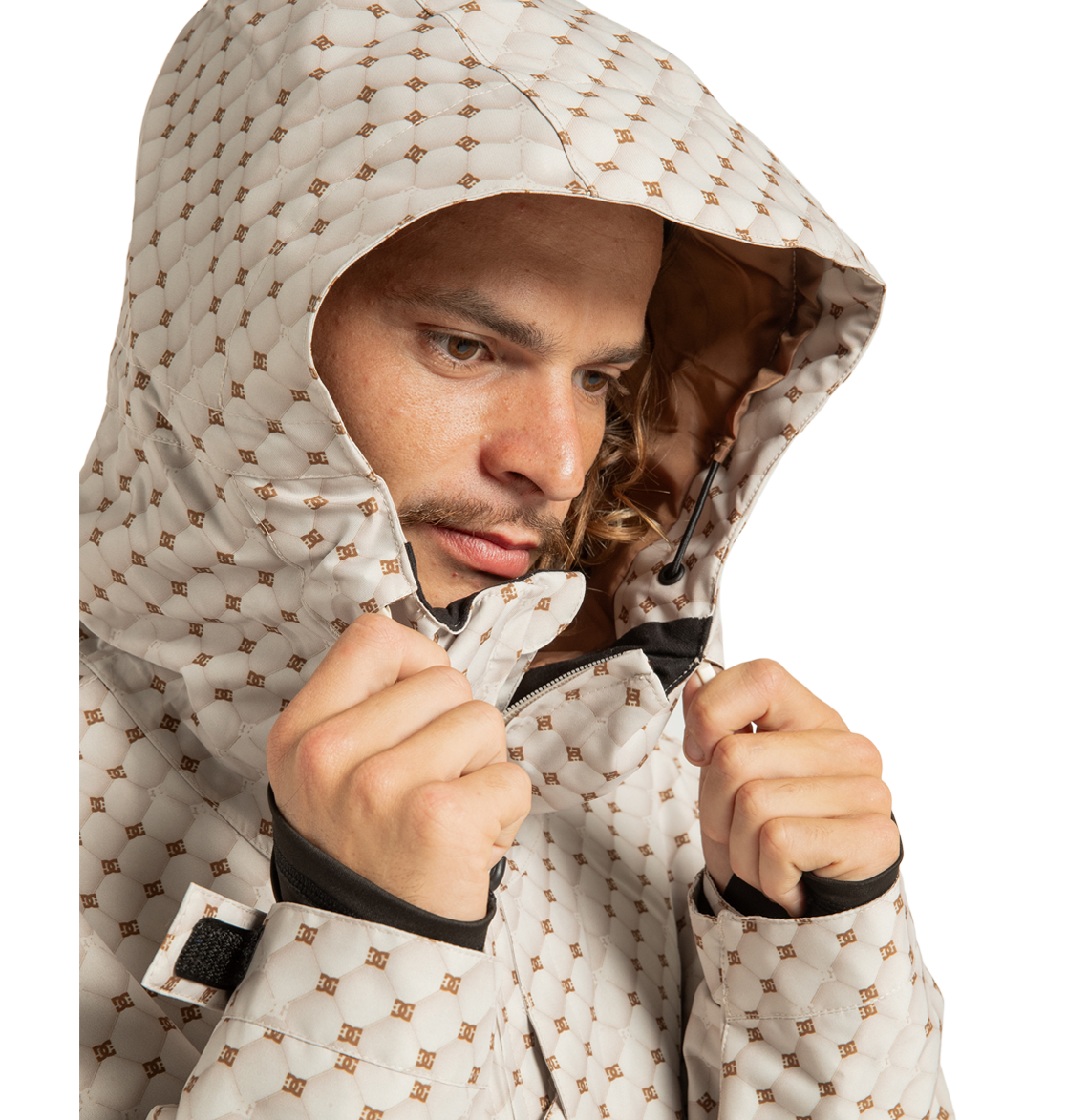 A person wearing the DC Shoes Unisex Basis Print Insulated Jacket, made from recycled polyester, zips up the light-colored geometric print hooded jacket while looking down and slightly to the side, with the hood pulled over their head.