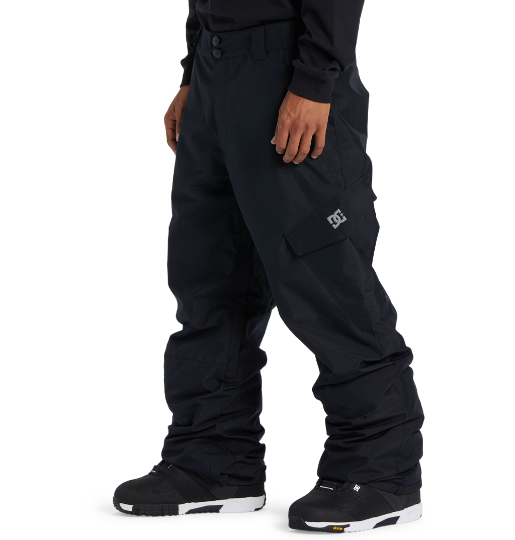A person is wearing loose-fitting black DC Shoes Men’s Banshee Insulated Pants, featuring a cargo pocket and a white DC logo, paired with black snow boots, and standing against a plain white background. These pants are an essential piece of winter gear designed to provide added warmth and comfort on cold days.