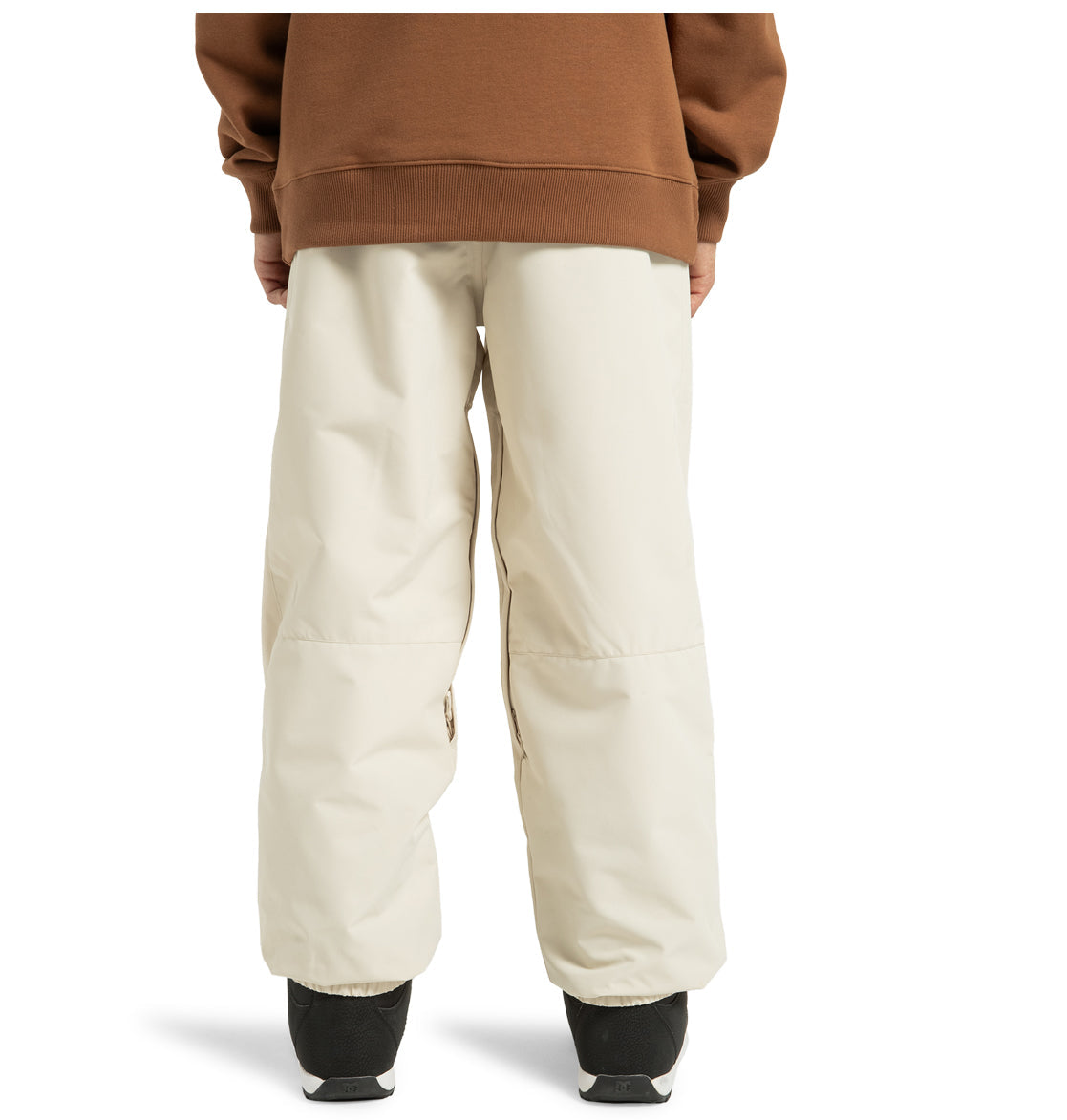 A person stands with their back to the camera, wearing a brown sweatshirt paired with DC Shoes’ Unisex Primo Snow Pants in a loose, off-white recycled polyester fabric. The wide-legged snow pants drape over black shoes.