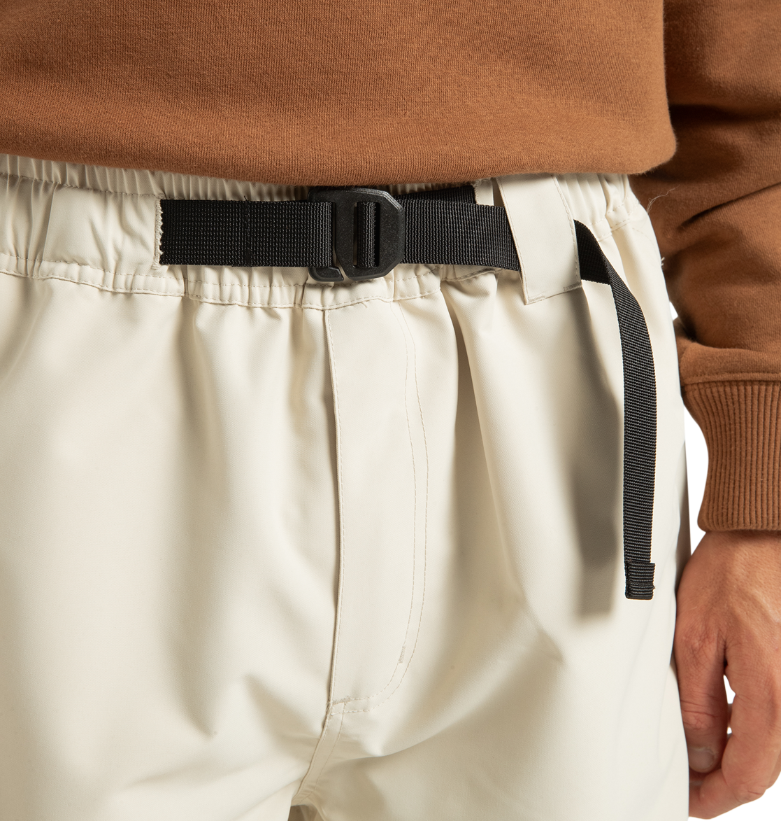 Wearing the Unisex Primo Snow Pants by DC Shoes in cream, featuring an elastic waistband with a black adjustable buckle belt and crafted from recycled polyester, styled with a brown long-sleeve top.