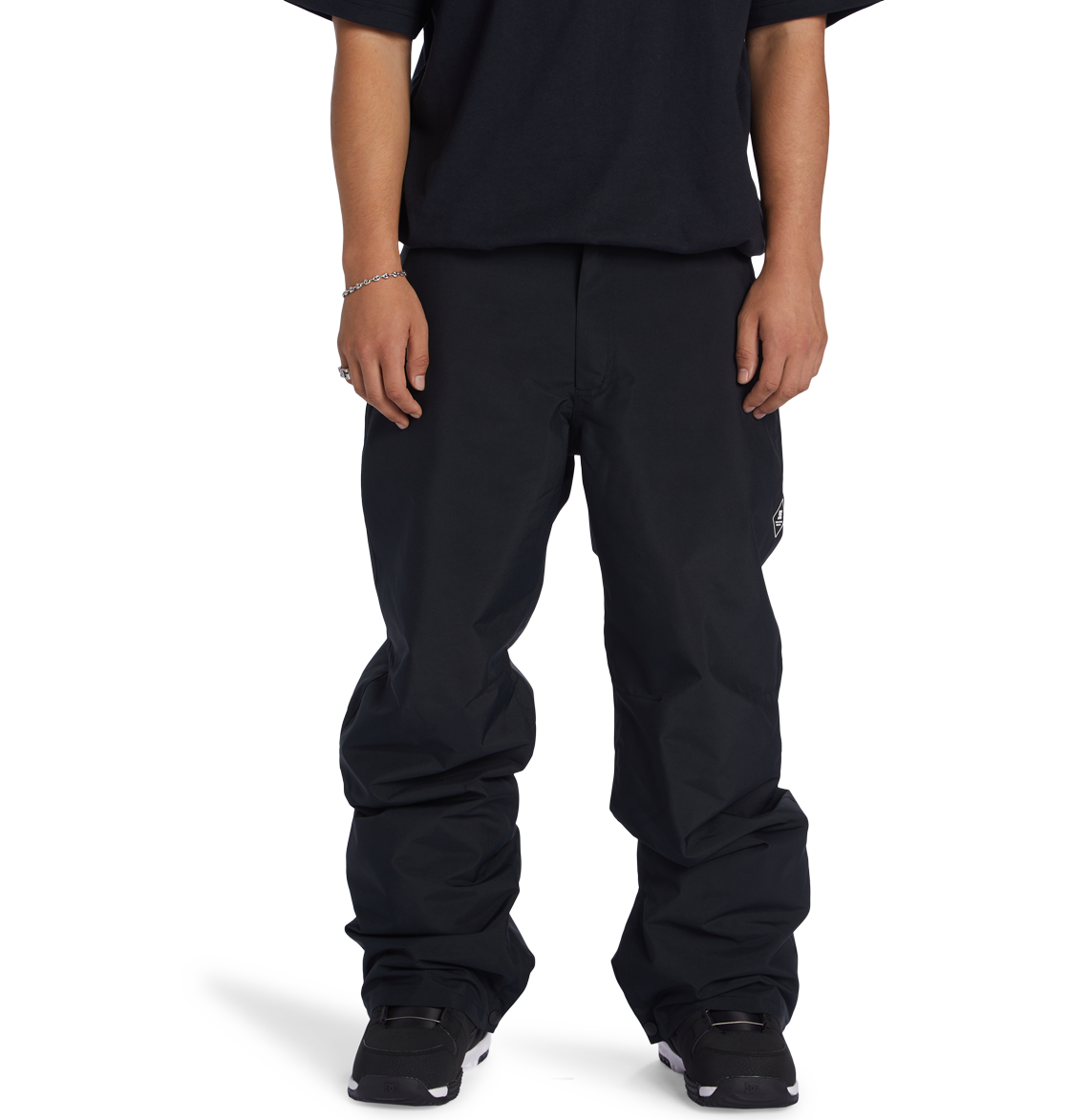 A person stands facing forward against a plain white background, wearing DC Shoes Men’s Insulated Chino Pants, a black T-shirt, black shoes, and a silver bracelet. Their face is not visible.