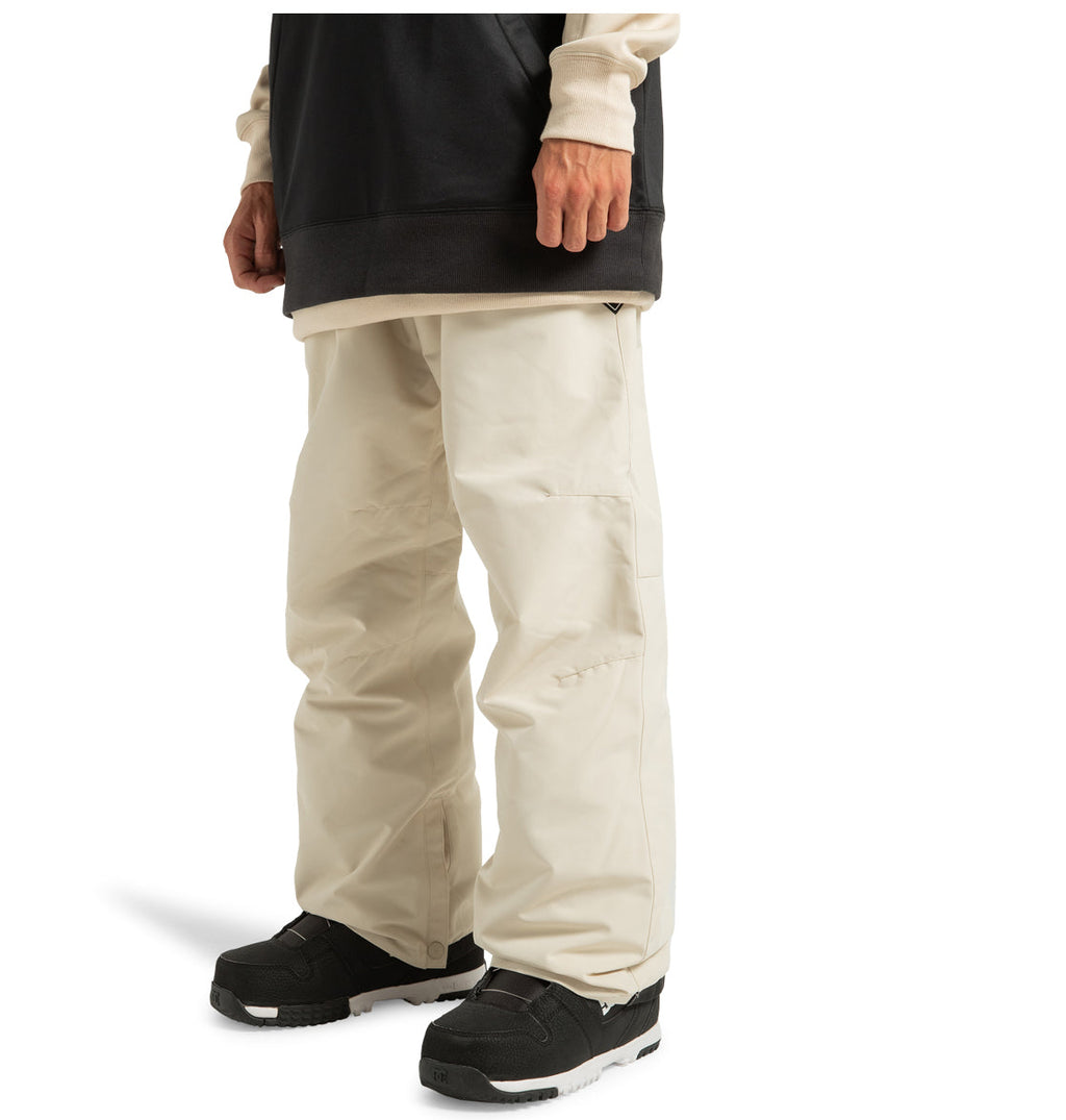 Model pictured from the shoulders down, wearing DC Shoes Men’s Insulated Chino Pants in off-white—crafted from recycled polyester with weather defense technology. Styled with a black and beige layered top and black snow boots, set against a white background.