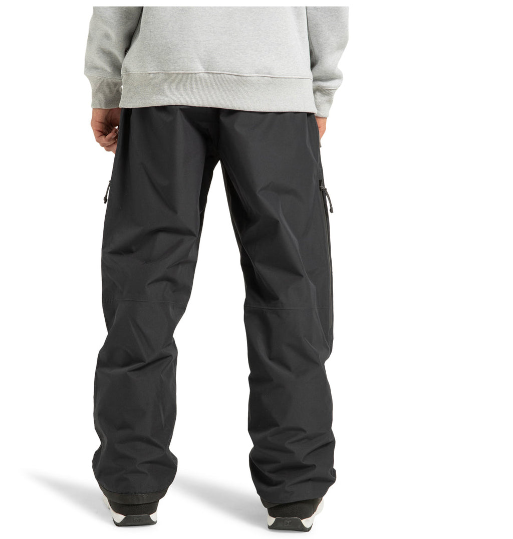 A person stands with their back to the camera, wearing a grey sweatshirt and loose-fitting black DC Shoes Unisex Squadron 30K Insulated Pants paired with dark shoes, against a plain white background—a look that ensures optimal weather defense and prepares you for any winter adventure.