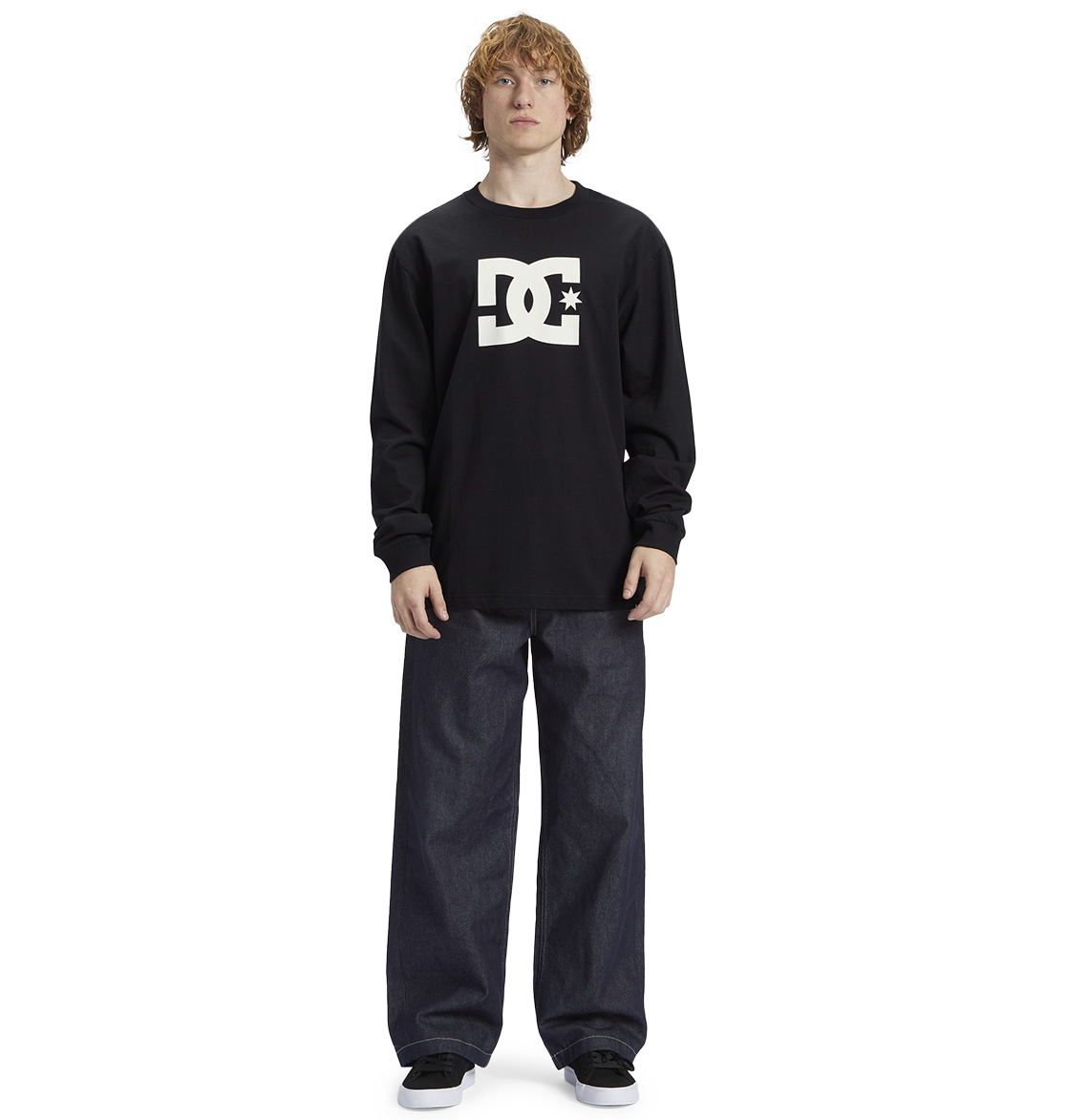 Young person with curly hair wears a black Men's DC Star Tee by DC Shoes, featuring bold graphics, paired with loose dark jeans and black sneakers, standing against a white background—ready to skate.