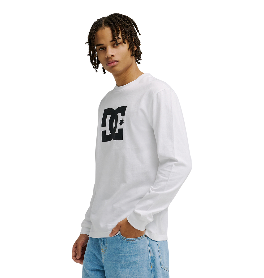 A person with short curly hair wears the Men’s DC Star Tee by DC Shoes, a white long-sleeve graphic shirt with a prominent black logo, paired with light blue jeans, standing against a plain white background.
