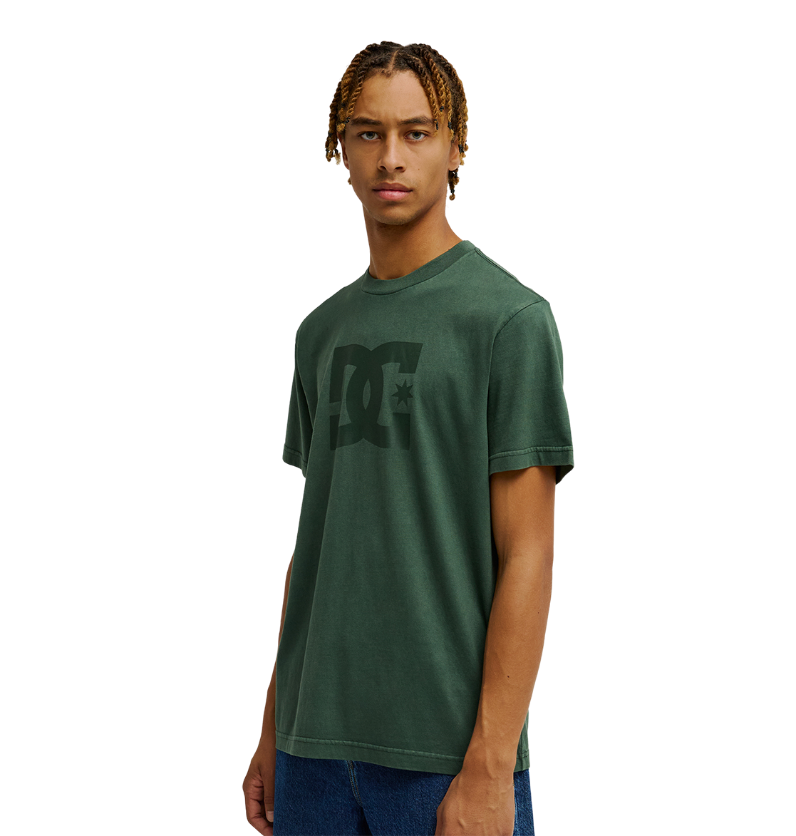 A person wearing the Men's DC Star Pigment Dye Tee by DC Shoes in dark green with a relaxed fit and blue jeans stands against a plain white background, looking straight ahead with a neutral expression.