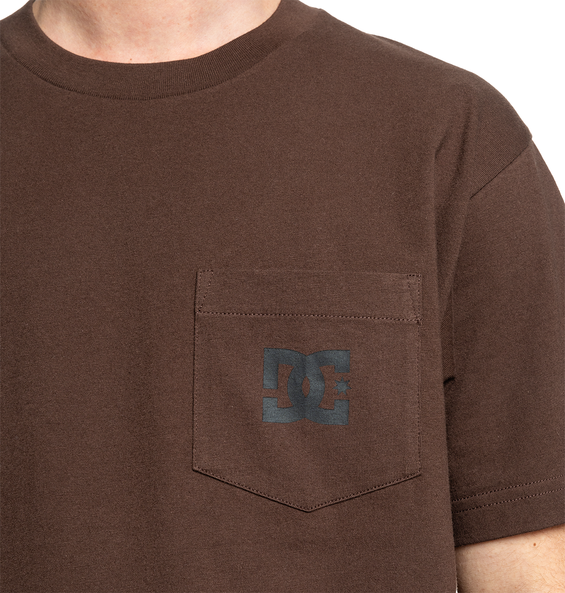 A person wears the Men's DC Star Pocket Tee by DC Shoes—a brown, relaxed-fit skate shirt with a small chest pocket and a dark gray DC logo. Only the upper torso is shown.