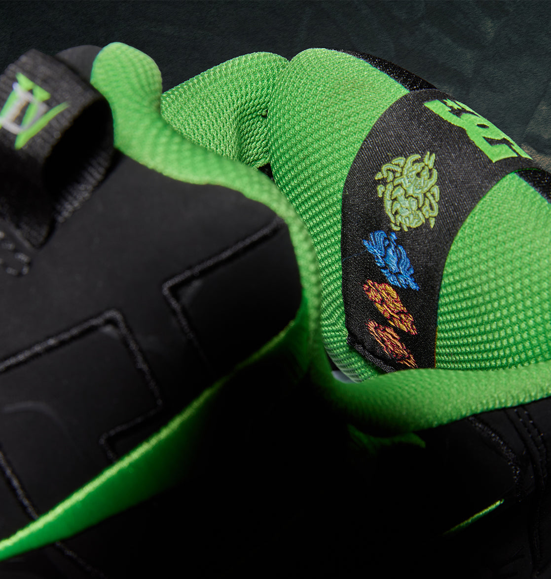 Close-up of a black and neon green Men’s Court Graffik x Diablo skate shoe featuring embroidered elemental symbols in green, blue, and orange on the padded tongue.