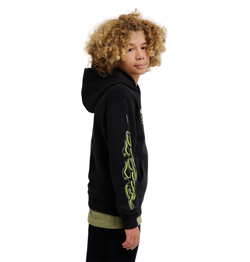 A youth model with curly blonde hair wears the DC Shoes Side Flame Hoodie, a black fleece featuring neon green flame designs on the sleeve, standing sideways and looking at the camera against a plain white background.