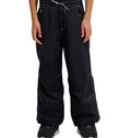 A person wearing loose black DC Shoes Trackstar Baggy Youth Pants with white stitching details, featuring a drawstring waist and snow performance waterproofing, paired with black sneakers, stands with hands relaxed at their sides.