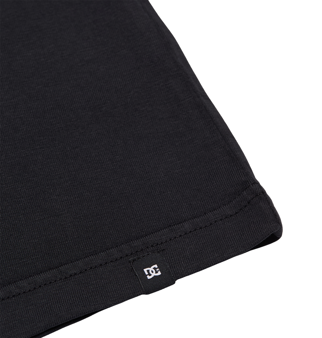 Close-up of the bottom hem of the DC Shoes Speratic Tee Youth skateboarding shirt in black, featuring a small black tag with a white DC Shoes logo, set against a plain white background.