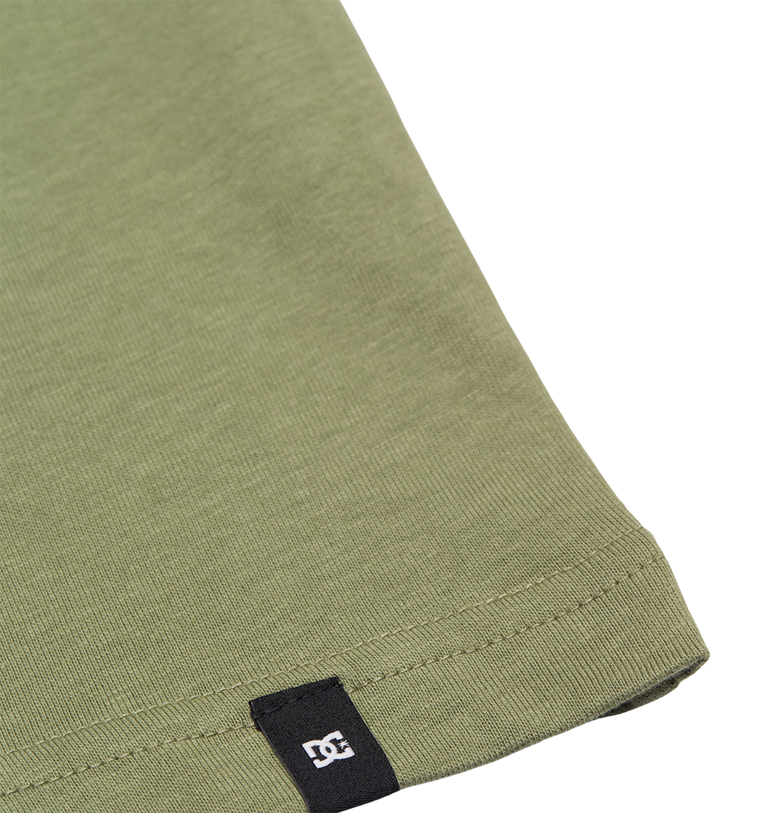 Close-up of the hem of the DC Shoes DC Star Filled Tee Youth in olive green, a relaxed fit t-shirt, featuring a small black tag with a white logo near the edge.