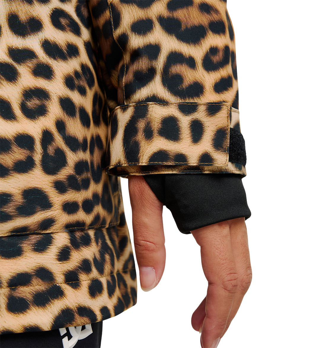 A close-up of a person’s hand wearing a black glove and the DC Shoes Cruiser Jacket, which features a brown and black leopard print pattern. The insulated sleeve of the Cruiser Jacket includes a strap with a black tab.