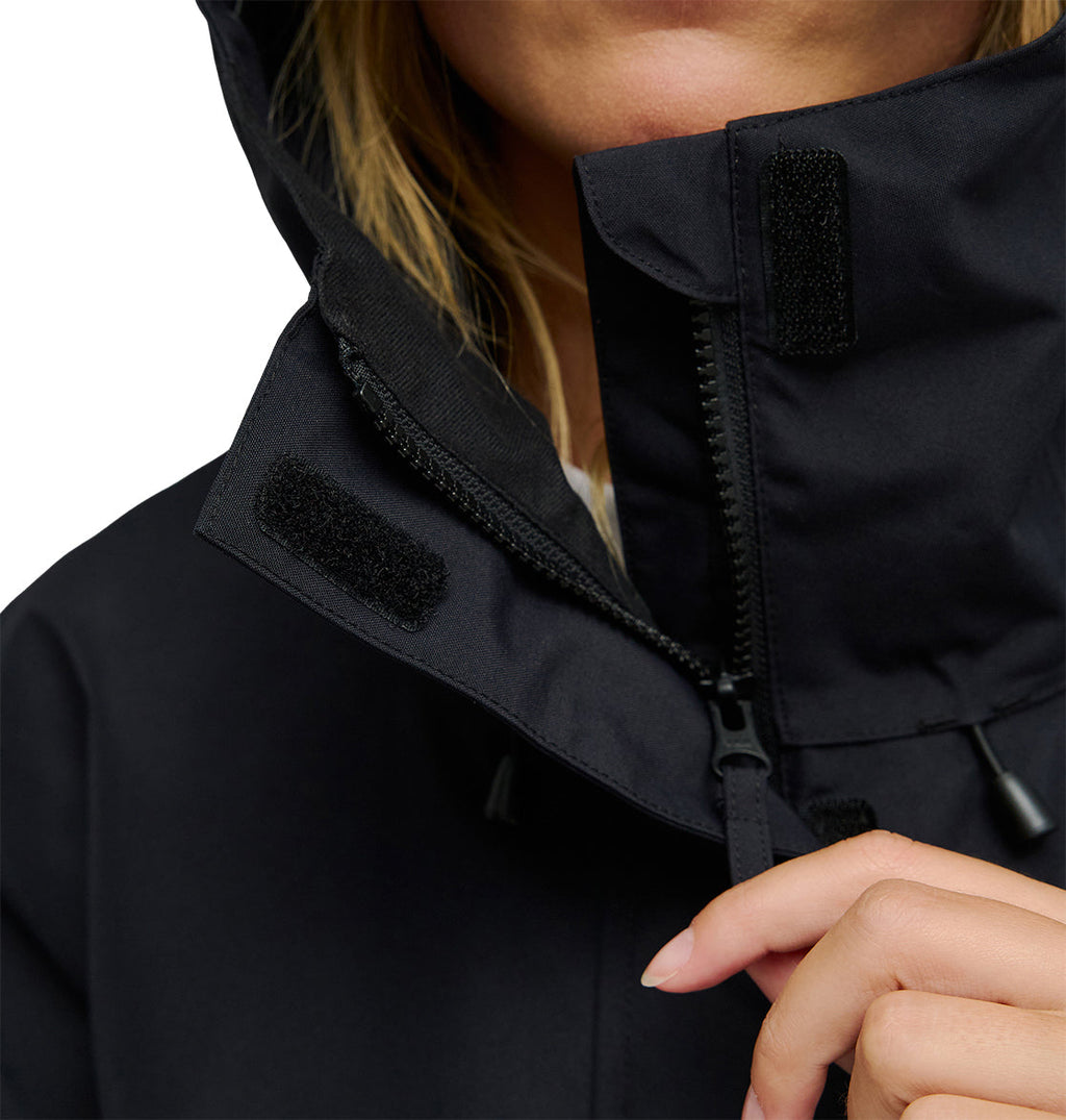 Close-up of a person zipping up the DC Shoes Cruiser Jacket, a black insulated style featuring Velcro patches on the collar. The person’s hand holds the zipper, with part of their face and blonde hair visible.