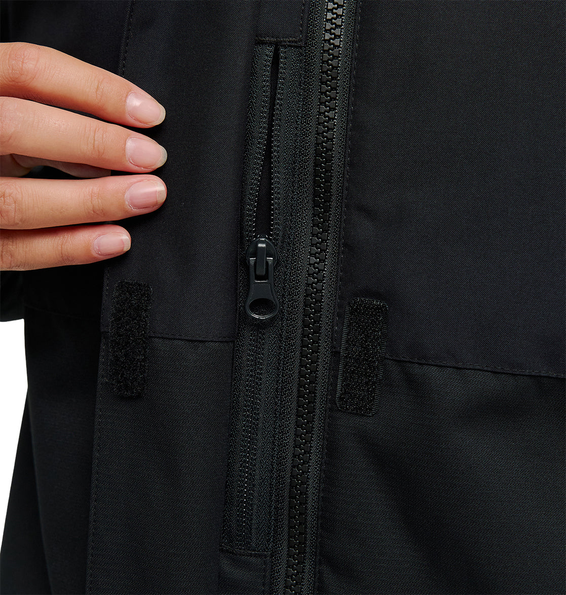 A close-up of a hand touching the chest area of the black DC Shoes Cruiser Jacket, highlighting the zipper and small Velcro patches.