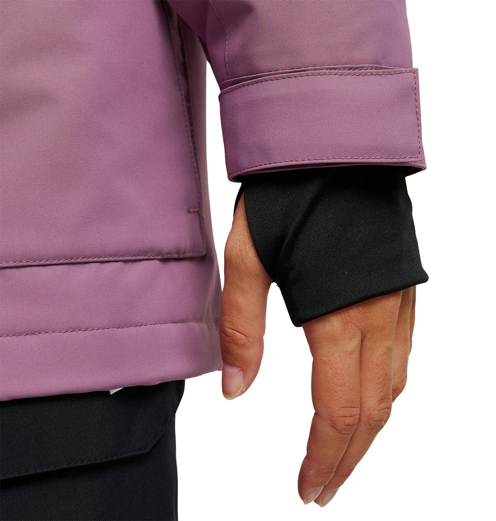 A close-up of a person’s hand wearing a black glove beneath the cuff of a purple DC Shoes Cruiser Jacket. The jacket sleeve features a velcro wrist strap, emphasizing its warm and protective design.