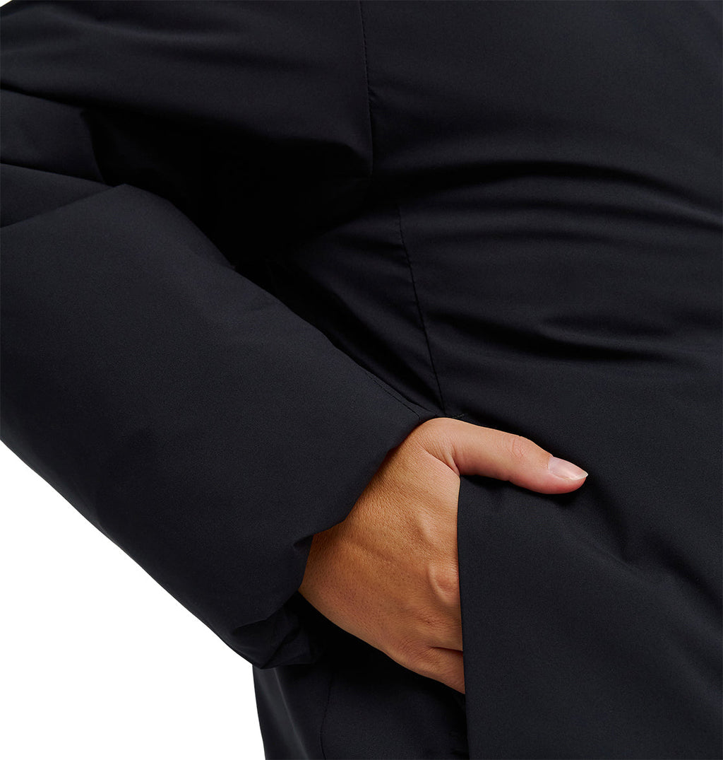 A person wearing the DC Shoes Aura Puffer Jacket in black slips their right hand into the jacket’s side pocket.