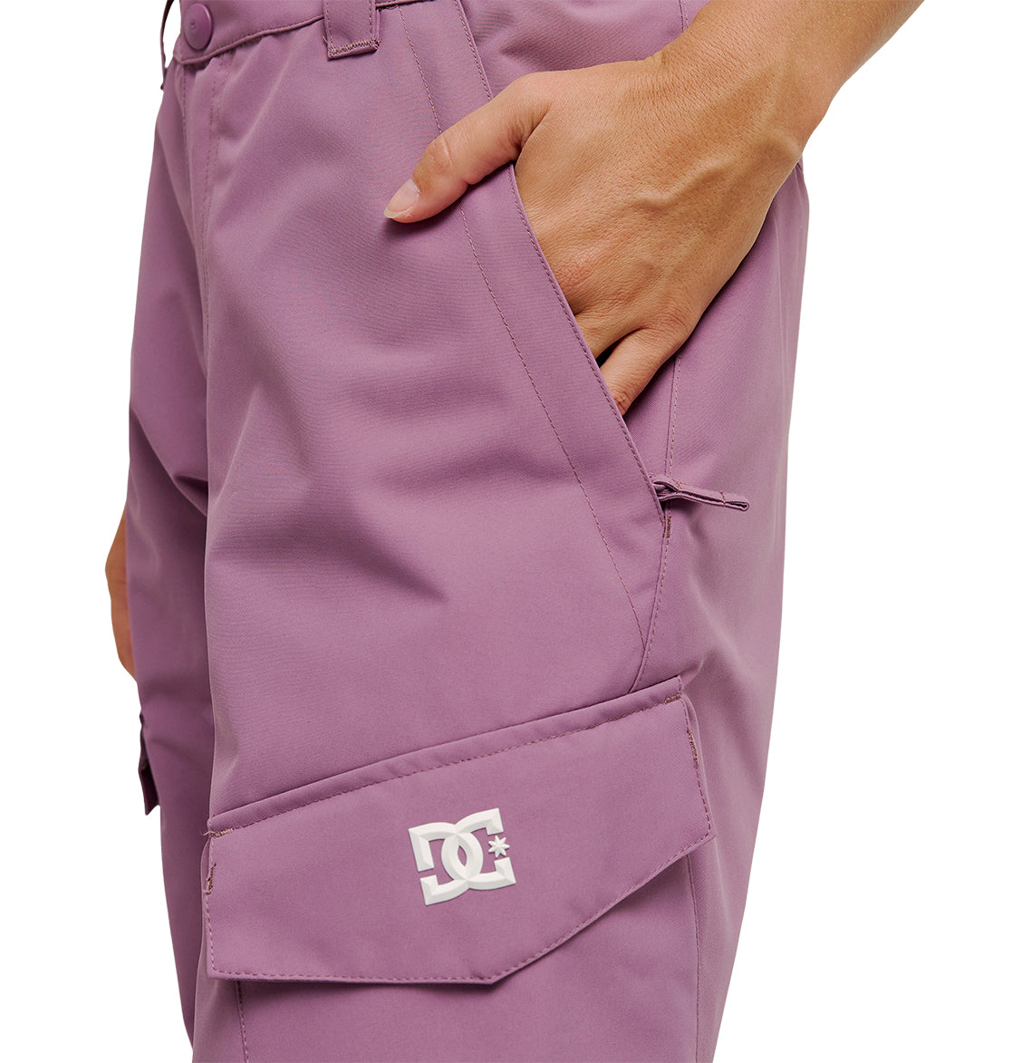 A person wearing the DC Shoes Nonchalant Pants in mauve, with a hand tucked into the pocket. These insulated cargo pants feature a DC Shoes logo on the flap of the side pocket and deliver enhanced snow performance for colder days.