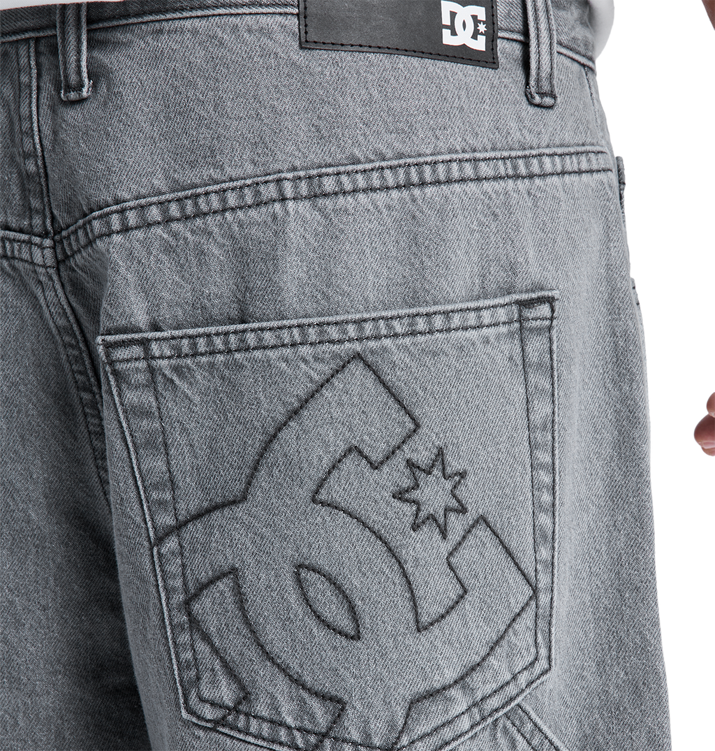 Close-up of the back pocket on DC Shoes Men's Baggy Denim Carpenter Pant in gray heavyweight denim, featuring a large embroidered logo and a black leather brand patch above the pocket, highlighting its wide-leg fit.