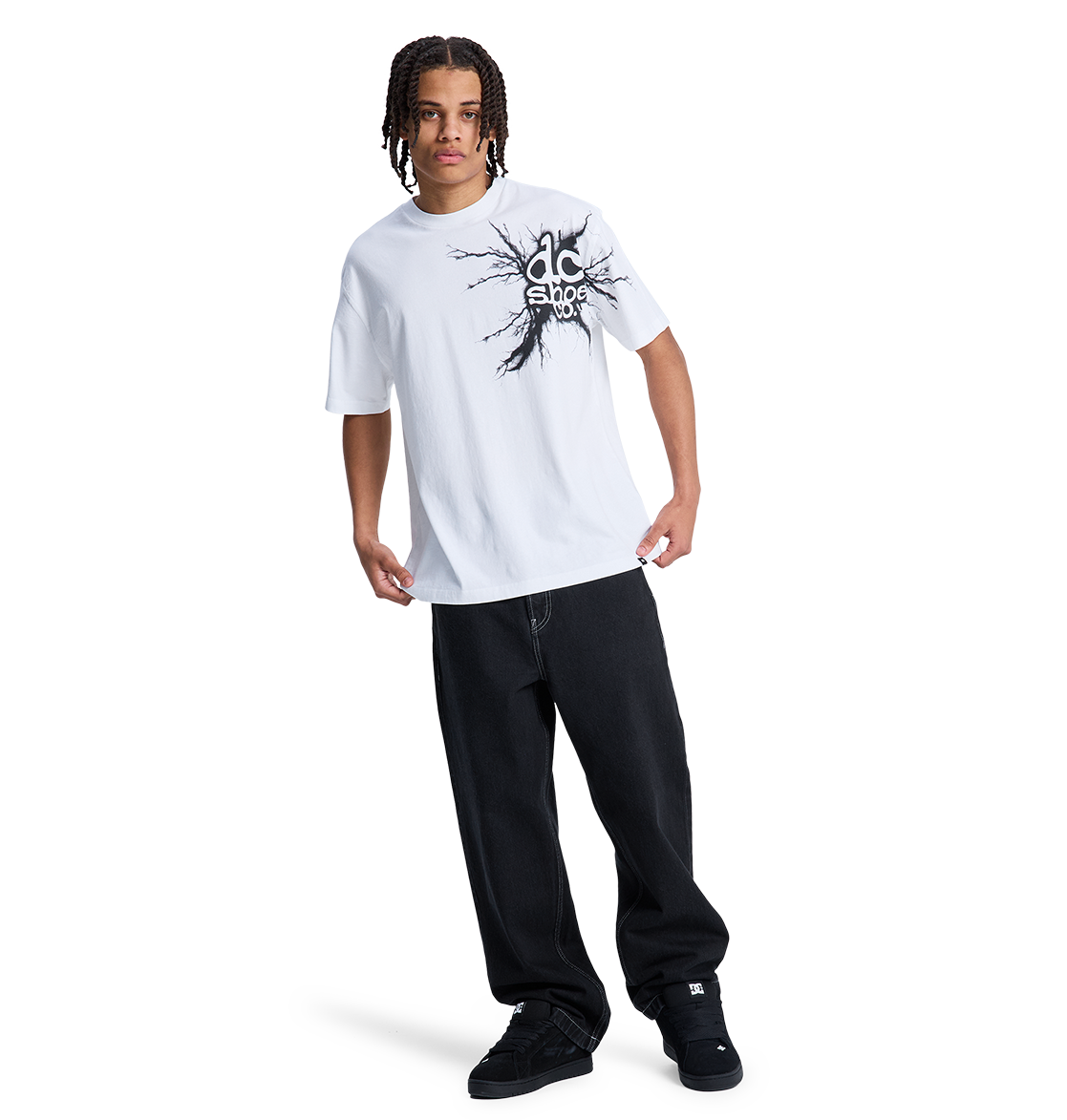 A person with braided hair wears a white graphic tee, black DC Shoes sneakers, and the Men's Baggy Denim Pant by DC Shoes, all set against a plain white background.