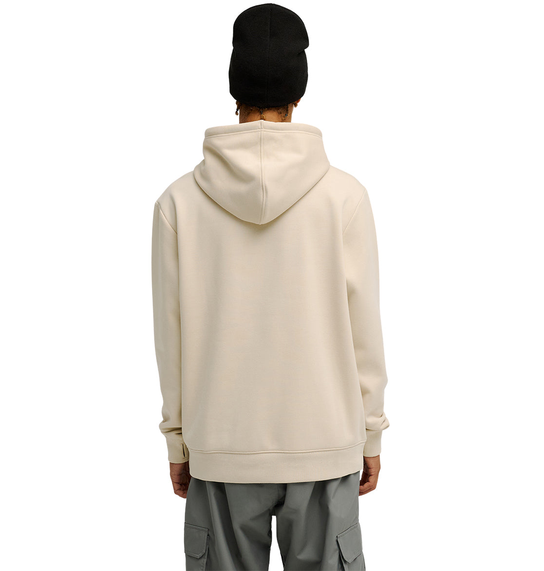 A person wearing the DC Shoes Snowstar light beige hoodie, paired with gray cargo pants and a black beanie, stands facing away against a plain white background.
