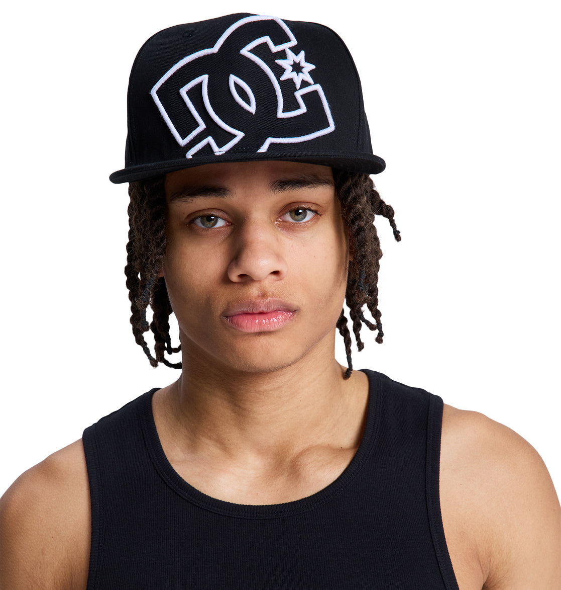 A person with long dreadlocks wears a black Reebok DC Double That Cap and a black tank top, looking directly at the camera against a white background.