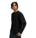 A person with short, curly hair stands against a plain white background, looking to the side, wearing a loose black T-shirt layered over the Men’s DC Twofer Long Sleeve by DC Shoes and paired with black jeans.