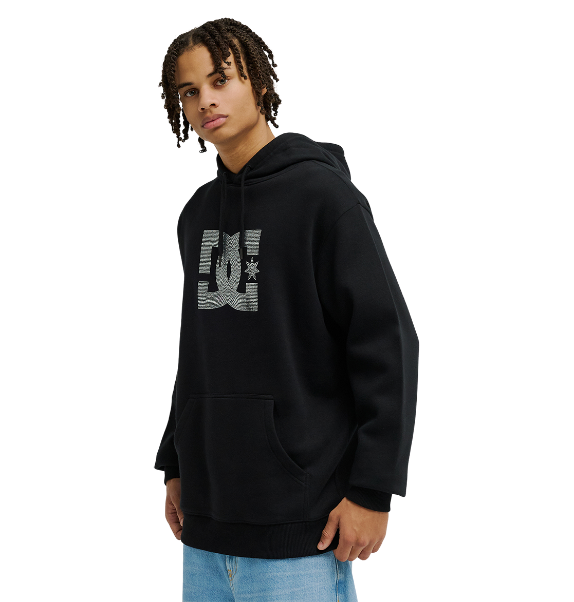 A person with short, curly hair models the Men’s DC Strass Star Hoodie by DC Shoes in black, paired with light blue jeans. Standing against a plain white background and gazing slightly to the side, they showcase the hoodie’s iconic DC logo and its blend of classic fleece warmth with modern style.