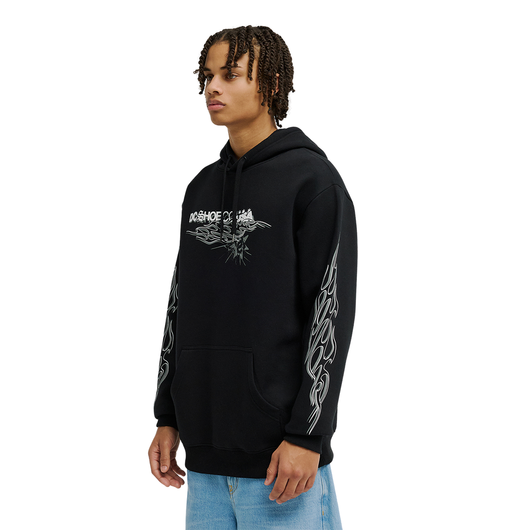 A person wearing the DC Shoes Men's Side Flame Hoodie, a black pullover with bold white DC graphics on the chest and sleeves, paired with light blue jeans, stands against a plain white background.