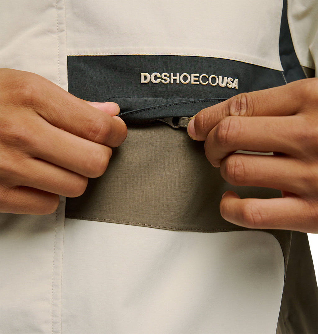 Close-up of hands opening a zippered pocket on the color-blocked Mountain Lab Jacket 20K by DC Shoes, featuring “DCSHOECOUSA” above the pocket and showcasing its breathable protection and dependable snow performance.