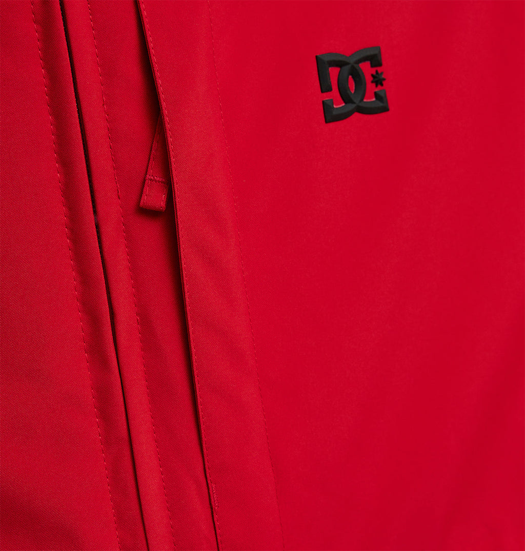 Close-up of the Basis Jacket 10K by DC Shoes, a red insulated jacket showcasing a black DC Shoes logo with a partially visible zipper along the left side.