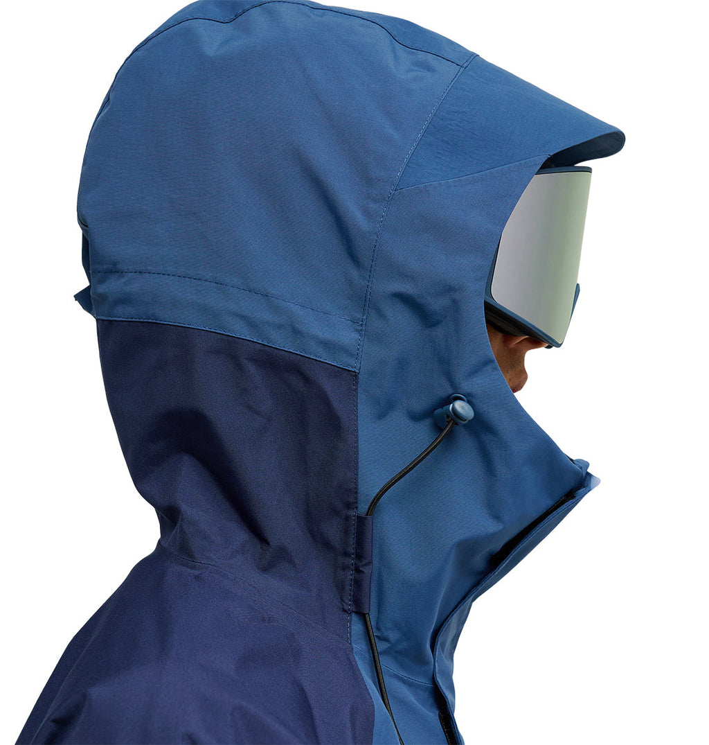 A person in profile wears the DC Shoes Mountain Lab Anorak 10K—a blue hooded jacket paired with ski goggles—set against a white background. The jacket offers breathable protection for comfort and optimal snow performance.