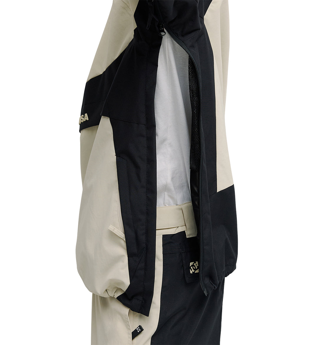 A close-up of the DC Shoes Mountain Lab Anorak 10K jacket in a beige and black color-block design, shown with matching pants and unzipped to reveal its mesh lining for breathable protection, displayed against a white background.