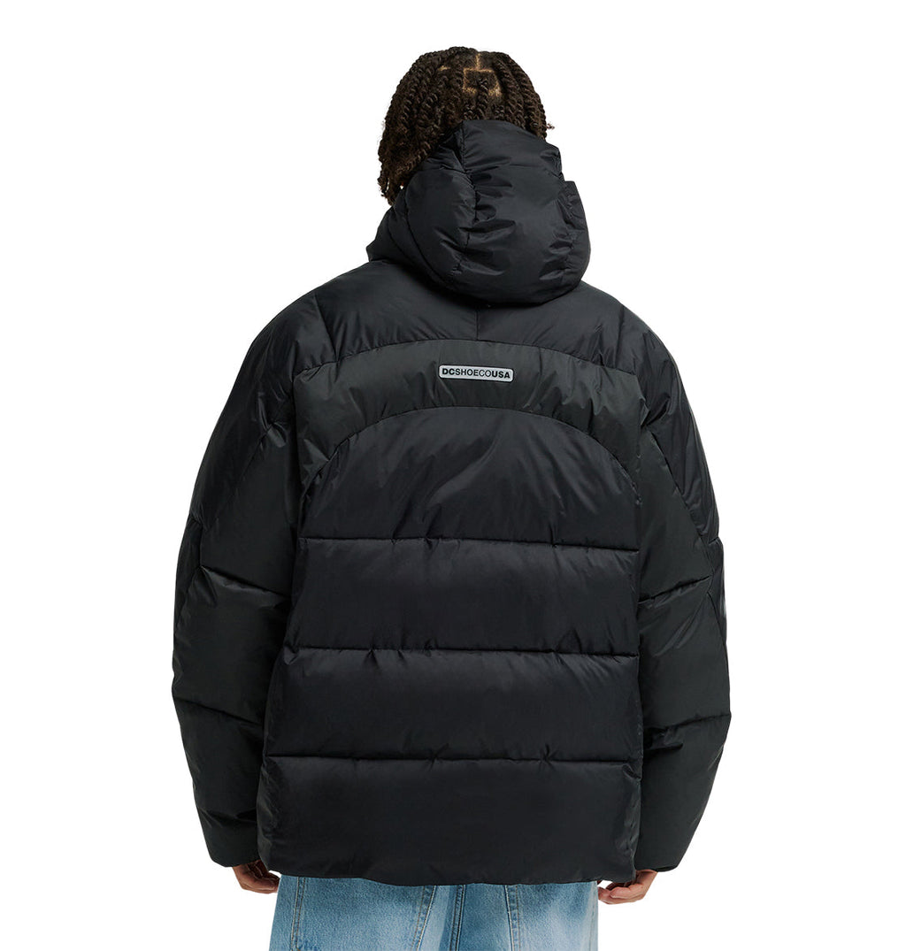 A person is seen from the back wearing the DC Shoes Powder Puffer 10K, a black hooded puffer jacket that provides breathable protection for all-day comfort. The jacket’s logo appears on the upper back. The outfit is completed with light blue jeans.