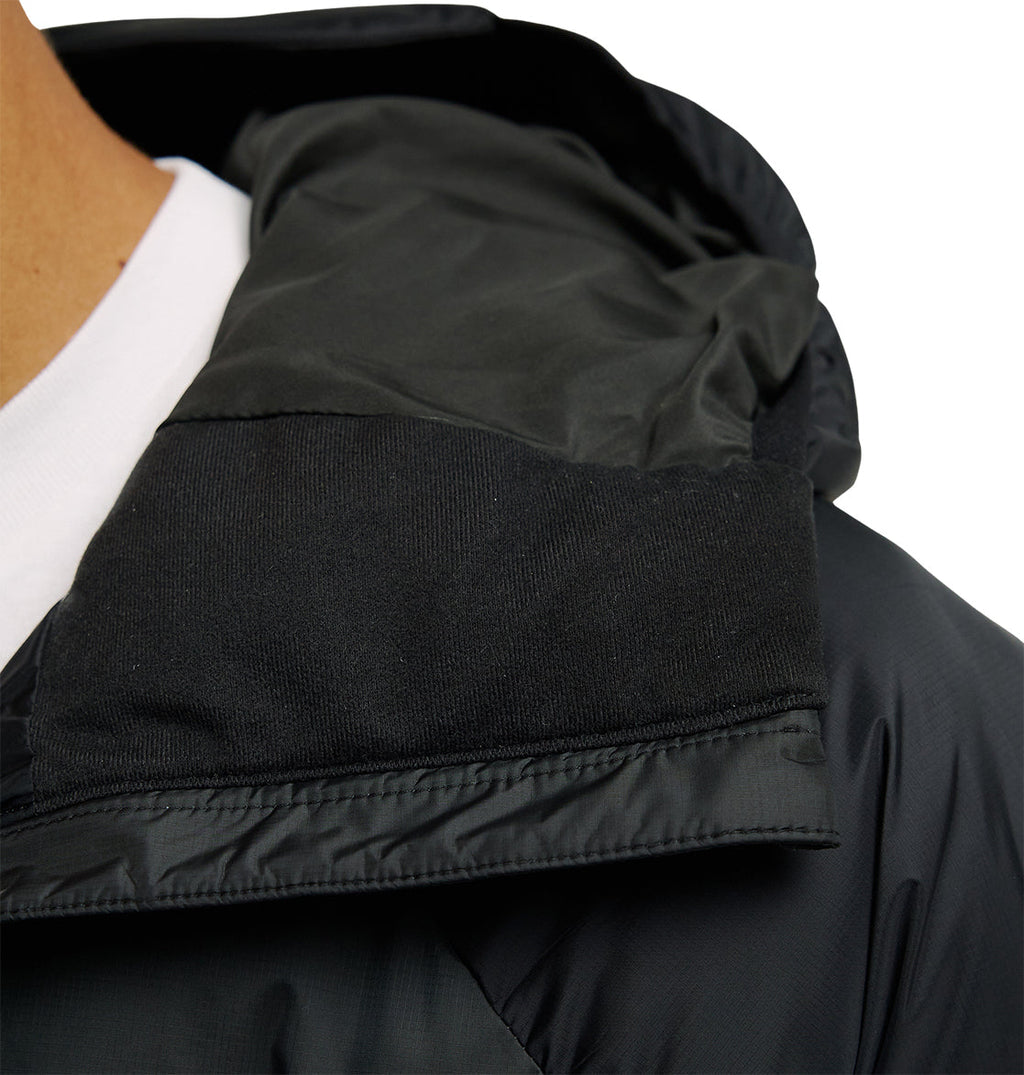 Close-up of a person wearing the DC Shoes Powder Puffer 10K black hooded jacket over a white shirt, highlighting the collar and hood area with visible fabric textures and stitching details that showcase its breathable protection, engineered for optimal snow performance.