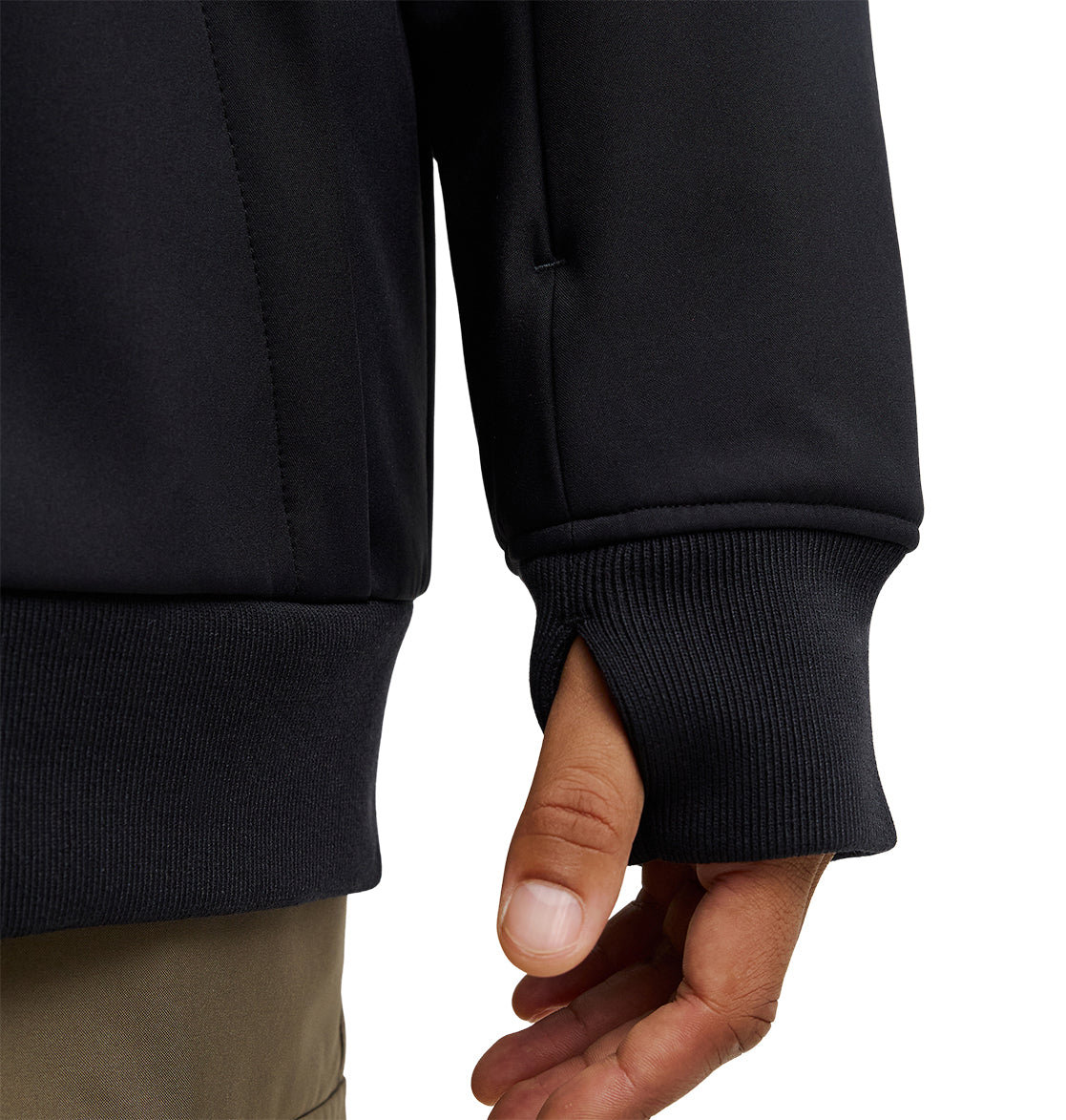 A close-up of a person’s hand partially inside the sleeve of the DC Shoes Spectrum Softshell Jacket, highlighting a thumb hole designed for added comfort and breathable protection. The person is wearing light brown pants.