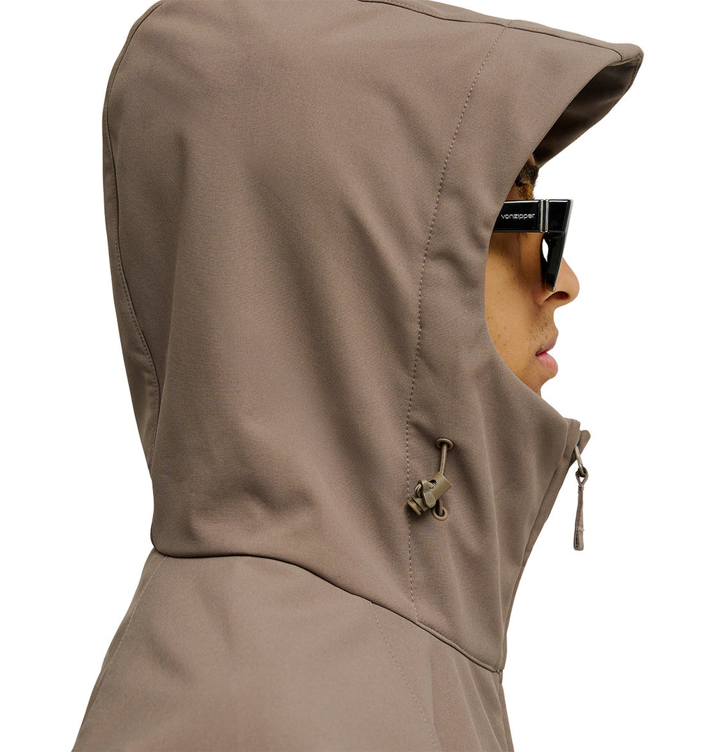 Wearing the DC Shoes Spectrum Softshell Jacket in taupe with the hood up and adjusted by its drawstring toggle, paired with black sunglasses—a perfect option for snow performance.