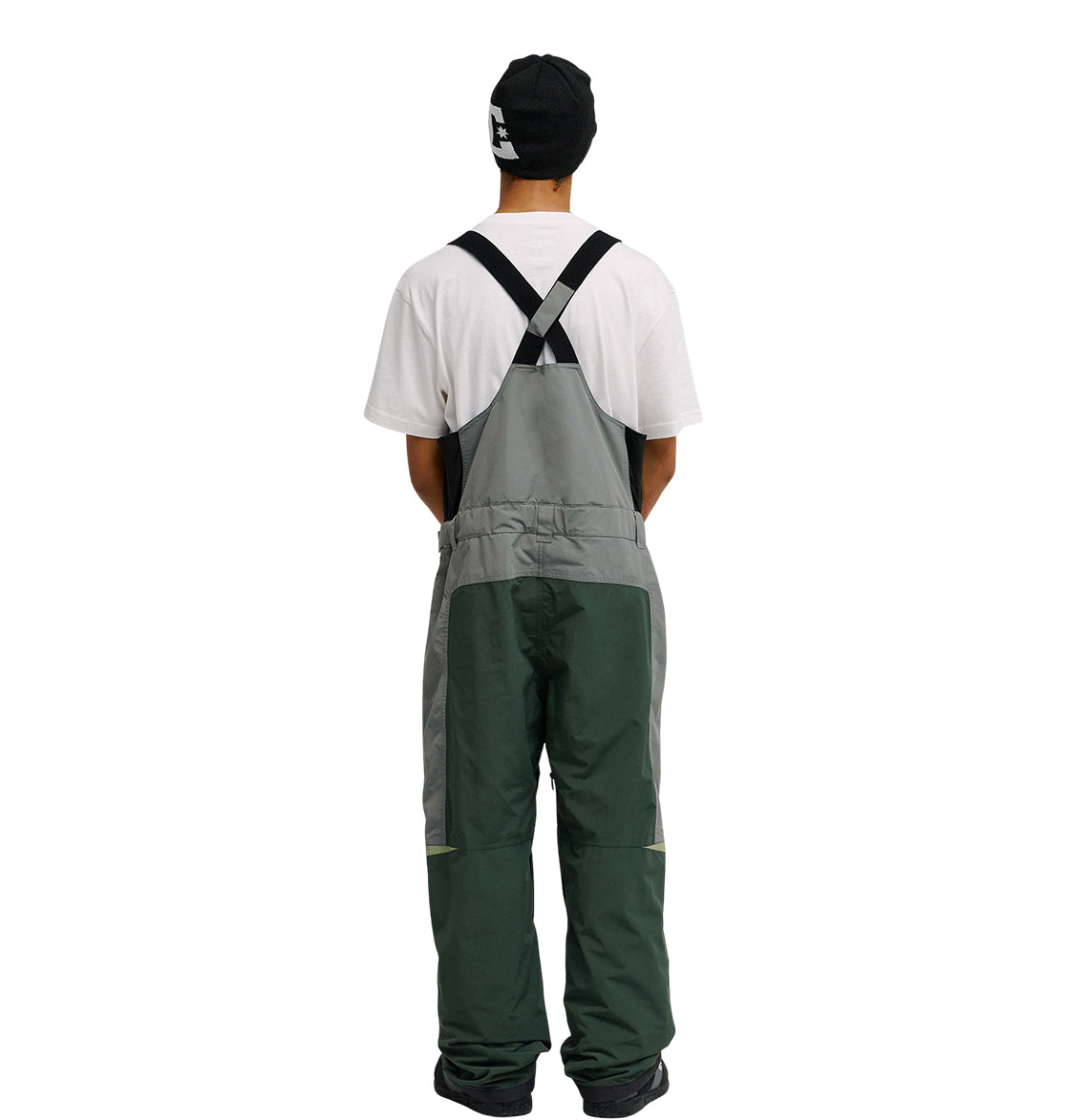 A person facing away, wearing a black beanie, white T-shirt, and DC Shoes Mountain Lab Bib 20K two-tone green overalls with black straps designed for breathable protection, standing against a plain white background.