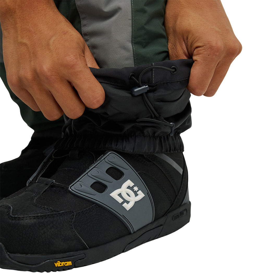 Hands adjusting black gaiters over black DC Shoes snow boots with Vibram soles, paired with Mountain Lab Bib 20K pants for breathable protection and enhanced snow performance.