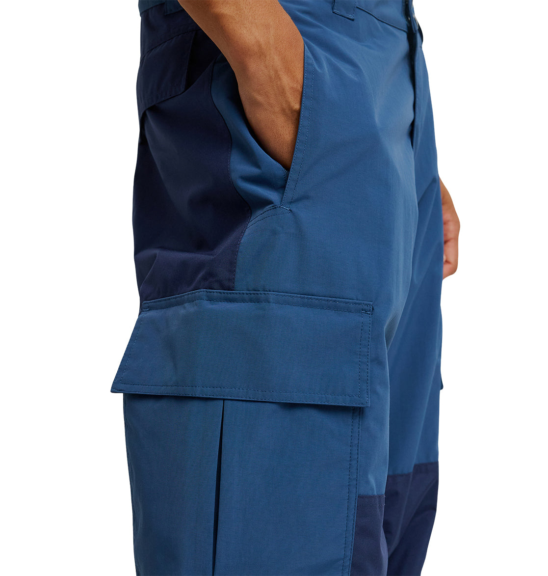 Wearing the DC Shoes Mountain Lab Pants 10K, a person stands with their right hand in the pocket. These waterproof pants showcase a large flap pocket on the thigh and feature dark blue panels running along the side and inside of the leg.