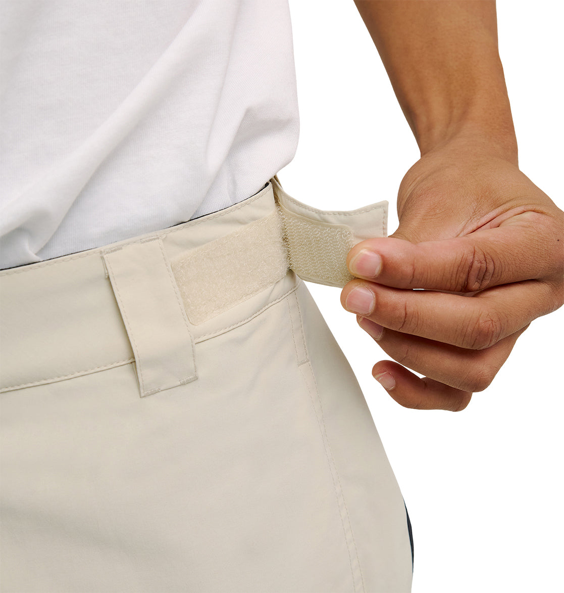Wearing a white shirt, a person adjusts the hook-and-loop (Velcro) waistband strap of light-colored DC Shoes Mountain Lab Pants 10K, ensuring a comfortable fit and optimal performance in the snow.