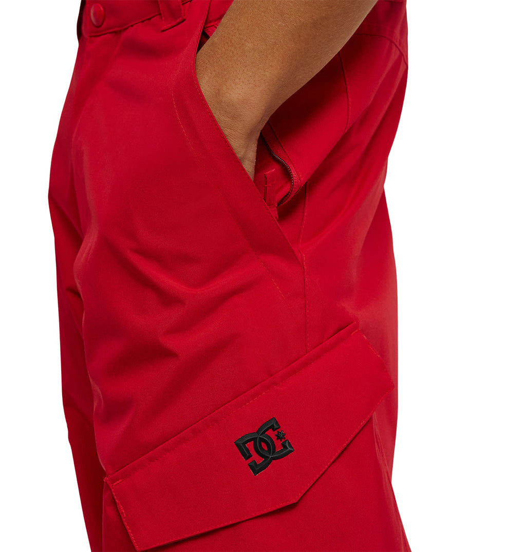 A person wearing bright red DC Shoes Banshee Pants with a hand in the pocket; the DC Shoes logo appears on a flap near the thigh.