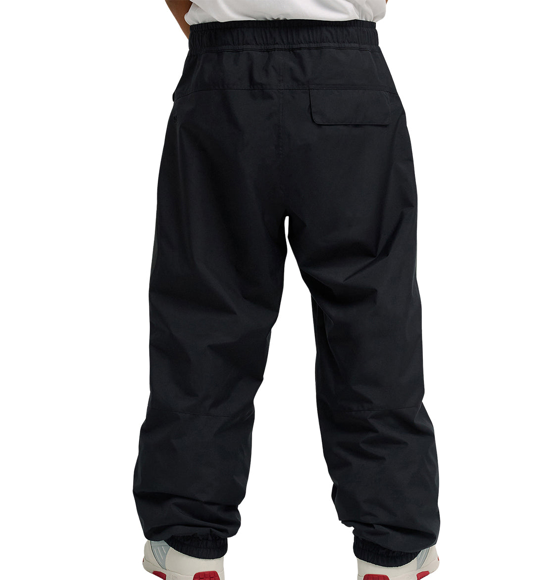 A person wearing DC Shoes Smoke Pants 10K—loose-fitting black pants designed for breathable protection—with white sneakers featuring red accents, shown from the back against a plain white background.