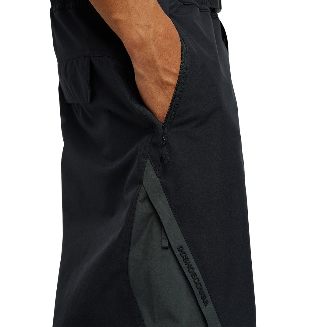 A person’s hand is in the pocket of DC Shoes Smoke Pants 10K, featuring black fabric with a diagonal zipper and gray accent, highlighting the detailed stitching and superior waterproofing design.